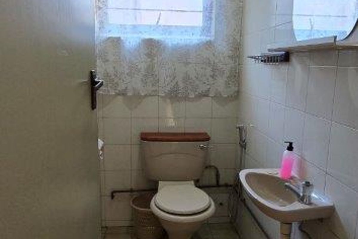 A compact, dated bathroom featuring tiled walls and floors, a wall-mounted basin, and a standard toilet, offering potential for modernization.