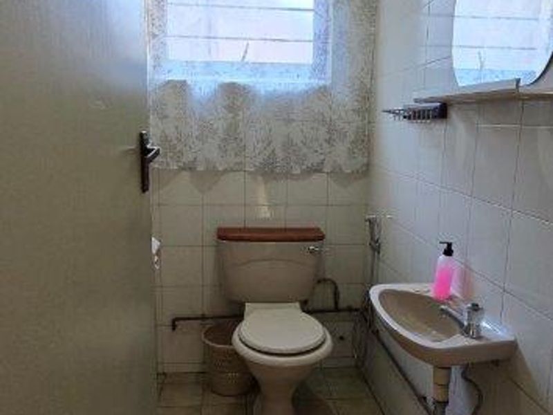 A compact, dated bathroom featuring tiled walls and floors, a wall-mounted basin, and a standard toilet, offering potential for modernization.