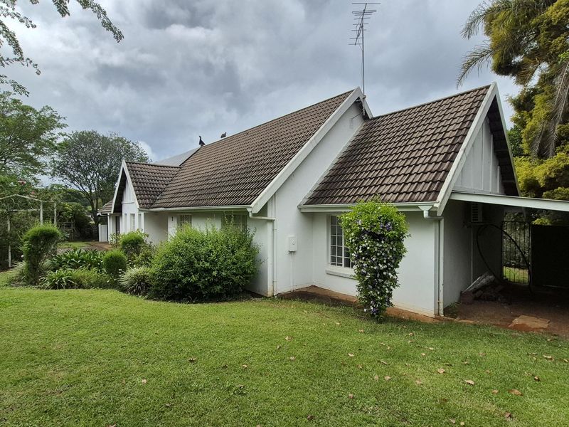A well-maintained rear exterior view of the house featuring a tiled roof, attached carport, and established garden surroundings.
