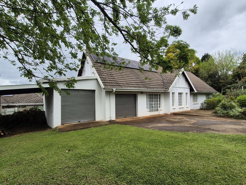Front exterior view of a house featuring a double garage, attached carport, solar panels on a tiled roof, and a paved driveway.