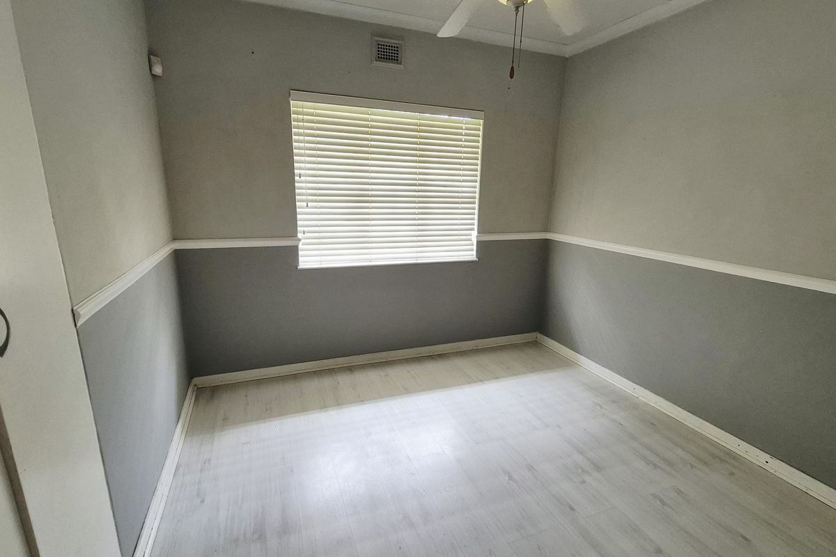 A clean, empty bedroom featuring light-toned laminate flooring, a built-in wardrobe, ceiling fan, and neutral two-tone wall paint with chair rail molding.