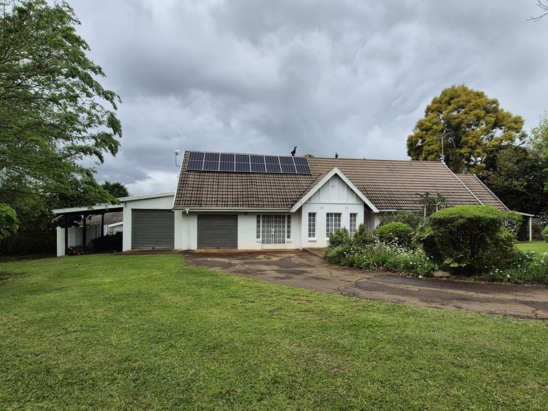 Front view of a residential property featuring a tiled roof with solar panels, a double garage, and a spacious front lawn with a paved driveway.