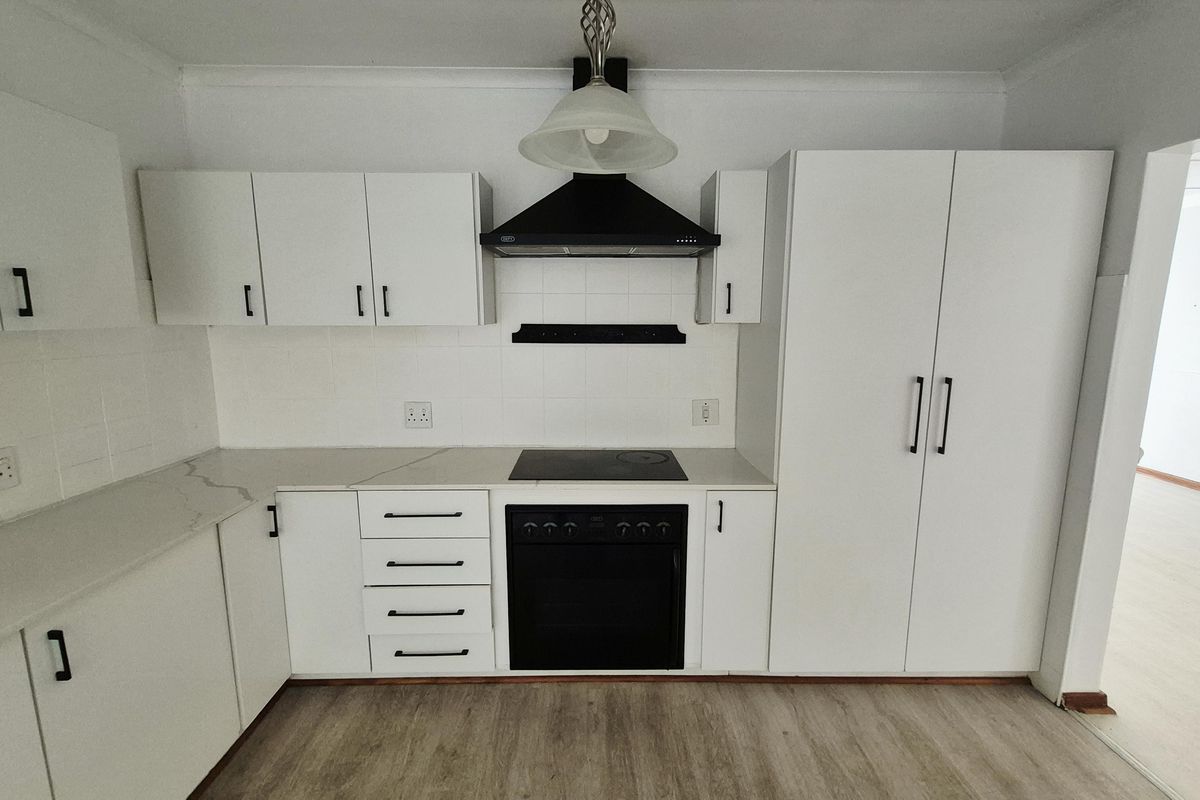 A clean, modern kitchen featuring white cabinetry, a built-in oven with electric hob, extractor fan, and light-toned laminate flooring.