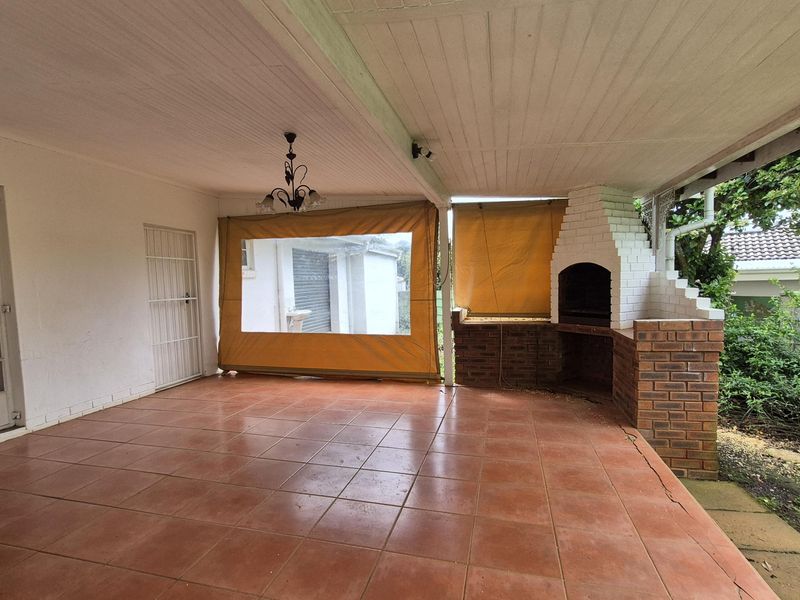 A spacious covered patio featuring a built-in brick braai, tiled flooring, and direct access to the home through a glass door.