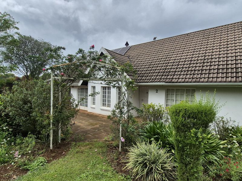 Rear view of the house featuring a tiled roof with solar panels, a paved patio area, and a garden with a decorative metal archway.