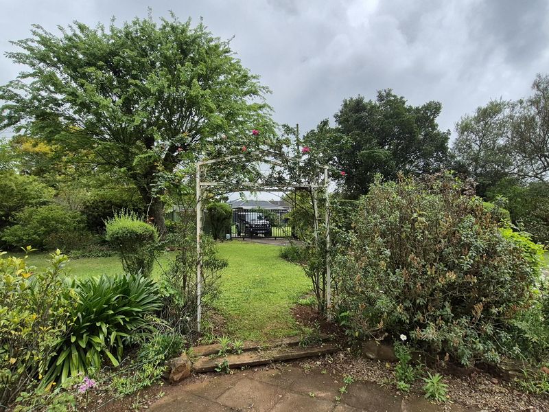 A lush, established garden featuring a decorative metal archway, stone paved area, and mature trees providing a private outdoor setting.