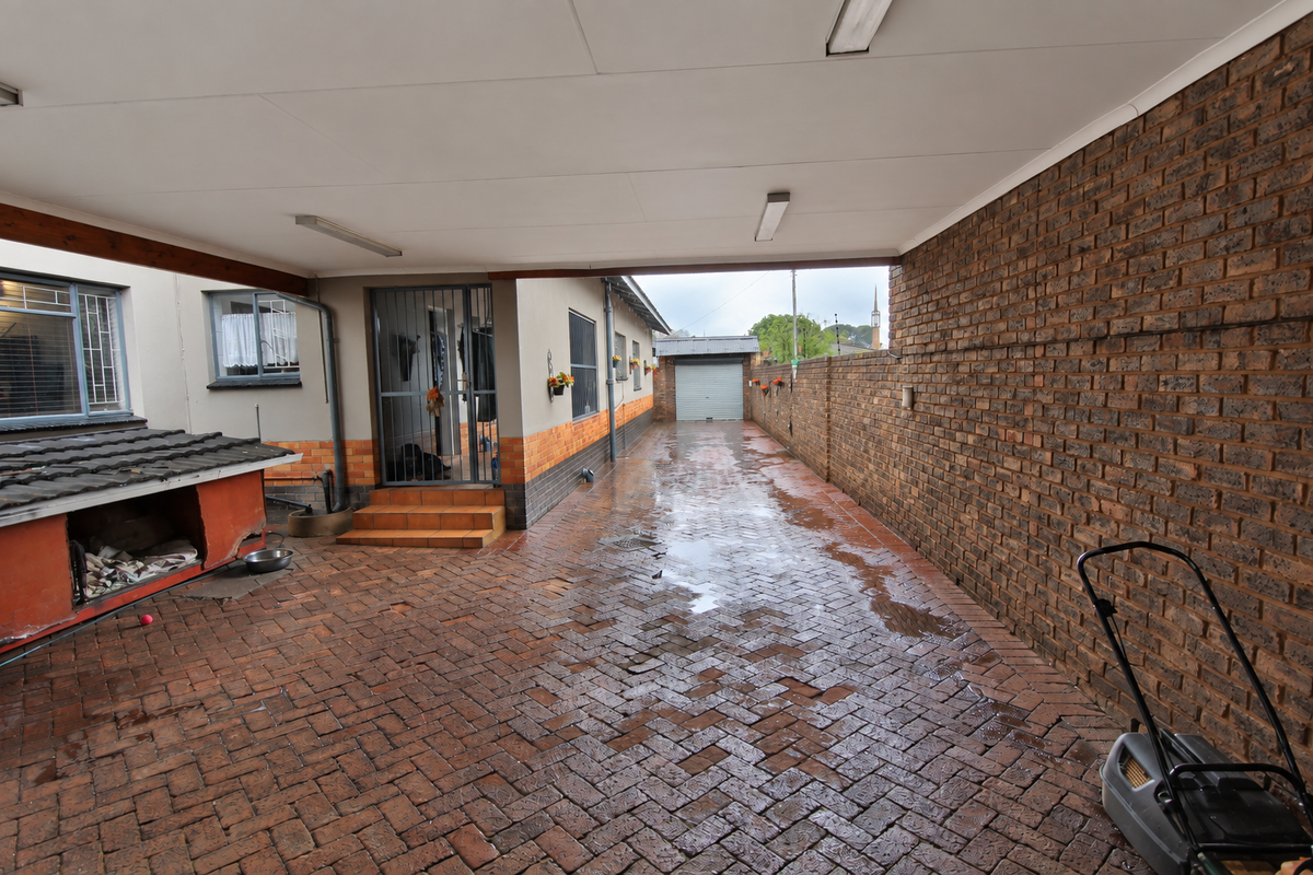 A covered rear patio area featuring brick paving, a long brick boundary wall, and access to a detached garage.