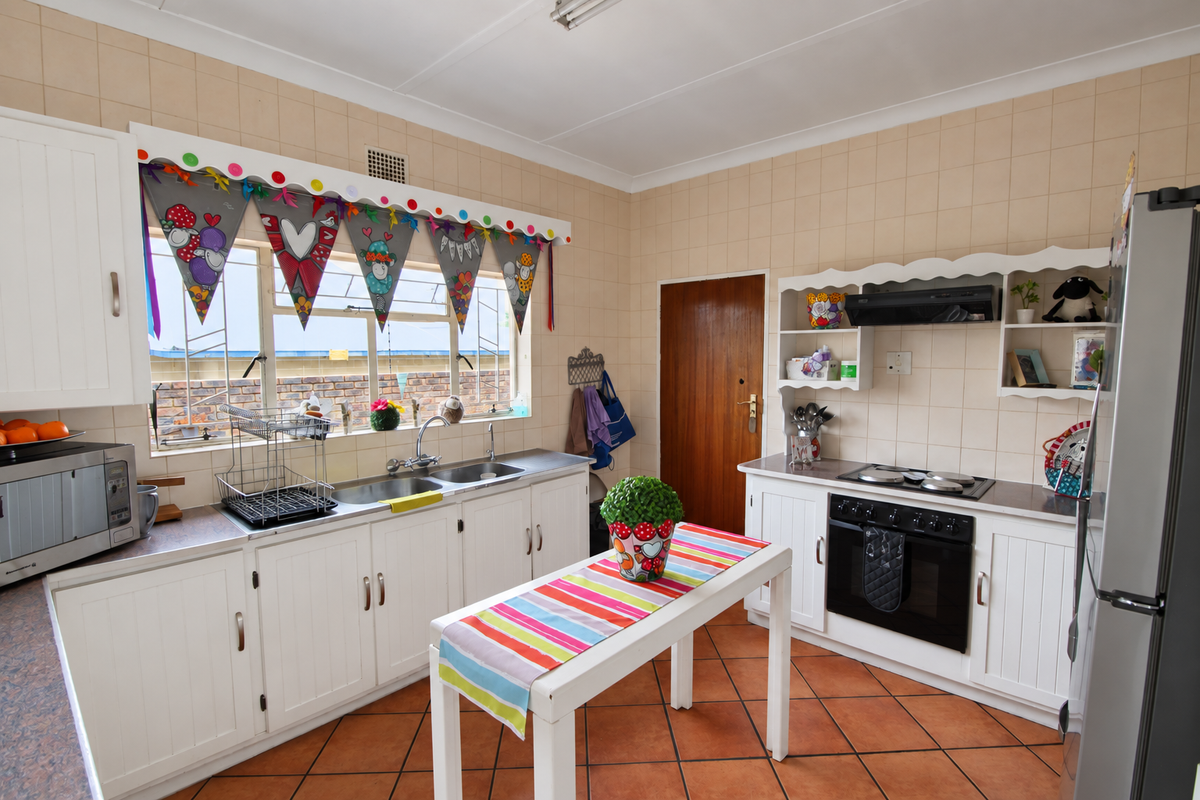A functional kitchen featuring white cabinetry, a double basin sink, built-in oven with hob, extractor fan, and tiled flooring throughout.