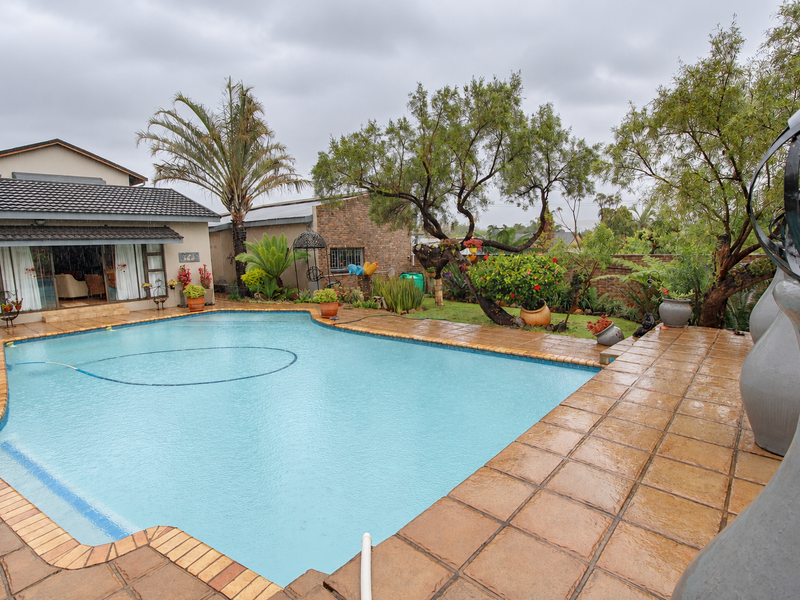A well-maintained outdoor pool area featuring a tiled deck, established garden landscaping, and direct access to the main residence via sliding glass doors.
