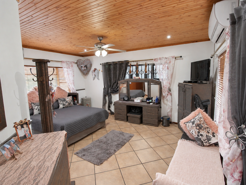 Spacious bedroom featuring a warm timber-clad ceiling, tiled flooring, and a wall-mounted air conditioning unit.