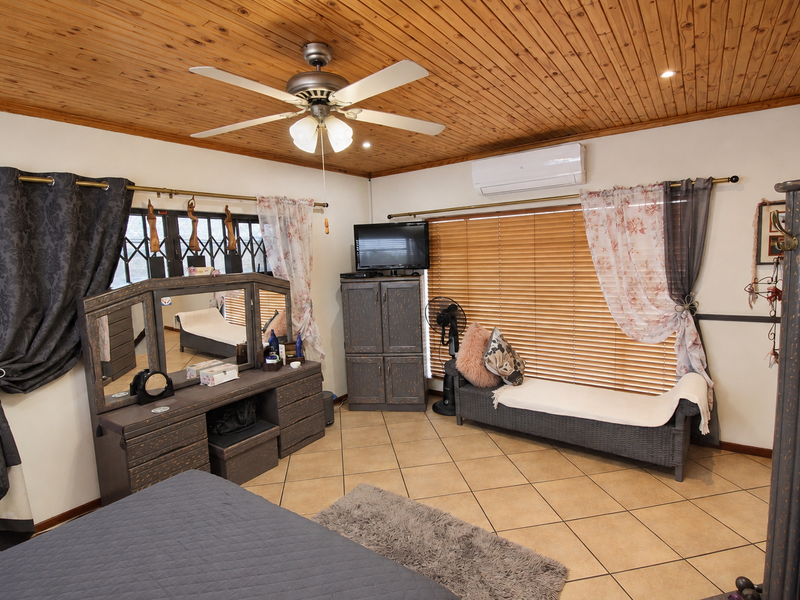 Spacious bedroom featuring a timber ceiling, ceiling fan, split system air conditioning, and ceramic tiled flooring with large windows and security gates.