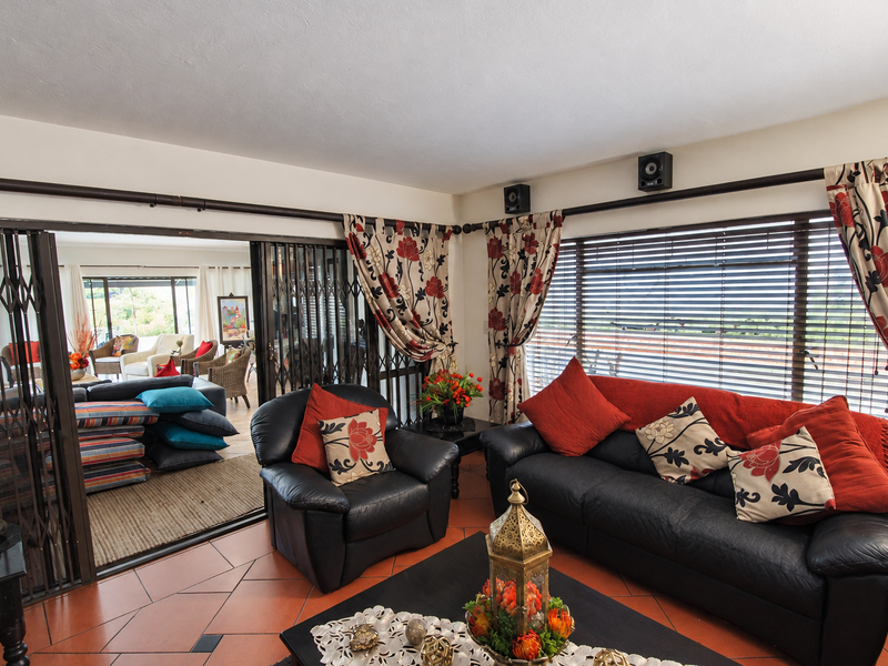 Open plan living area featuring terracotta floor tiles, large windows with venetian blinds, and sliding security gates leading to an adjacent patio space.