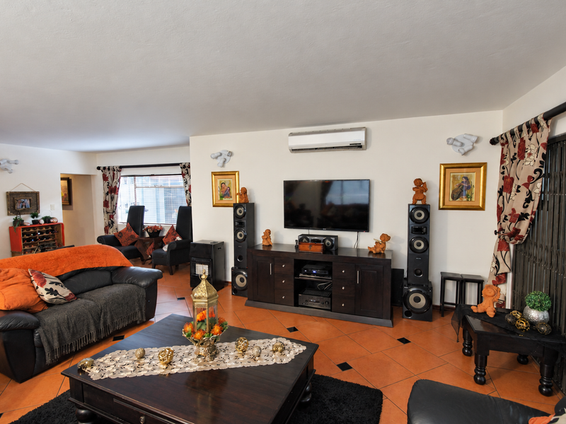 Spacious living room featuring terracotta floor tiles, a wall-mounted split-system air conditioner, and access to an outdoor area via a sliding security gate.