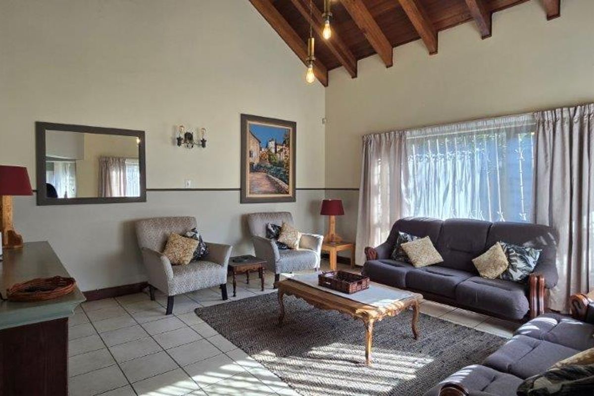 Spacious living room featuring a high vaulted ceiling with exposed timber rafters, tiled flooring, and large windows with curtains.