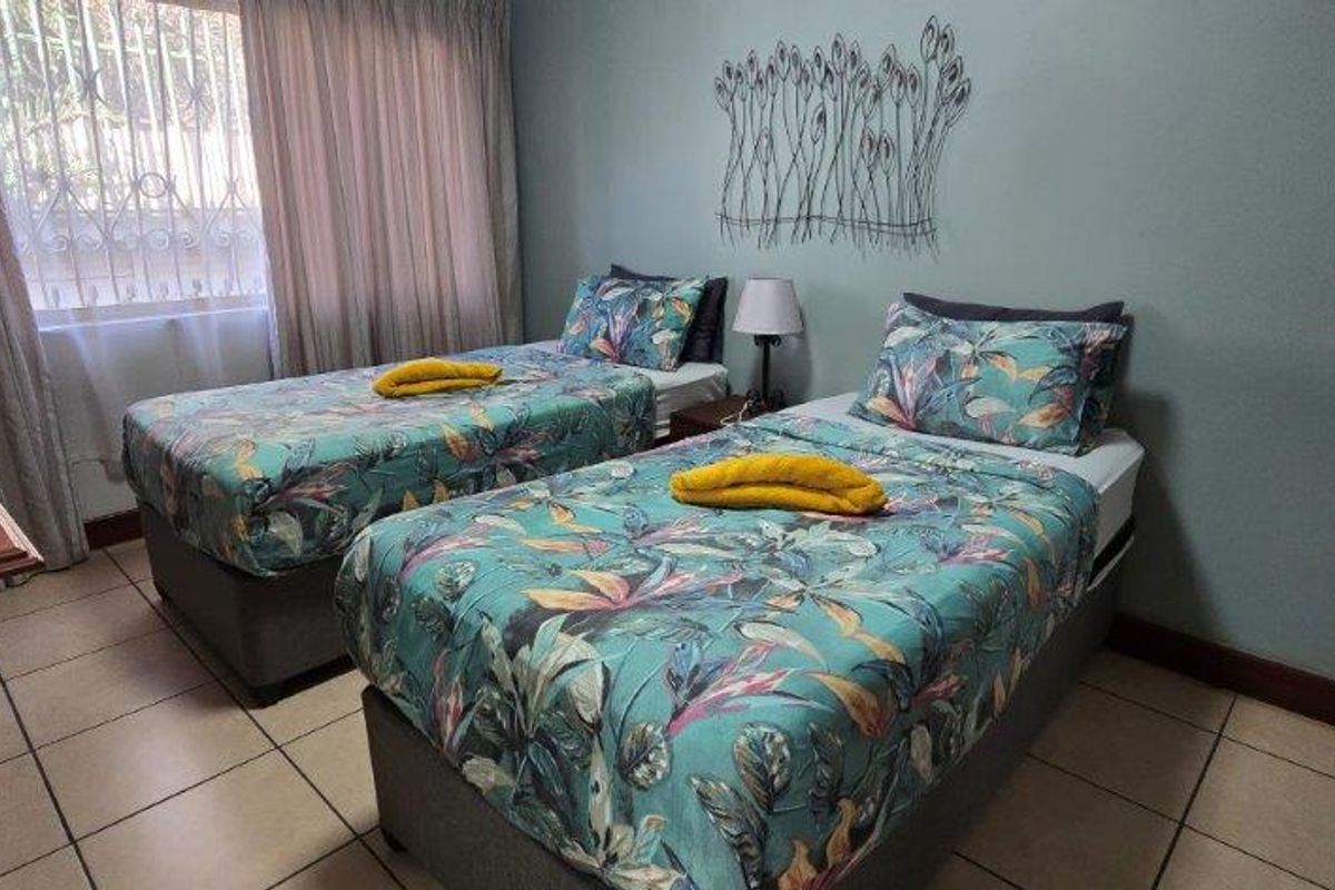 A functional bedroom featuring tiled flooring and a window fitted with security bars, providing a practical space for rest.