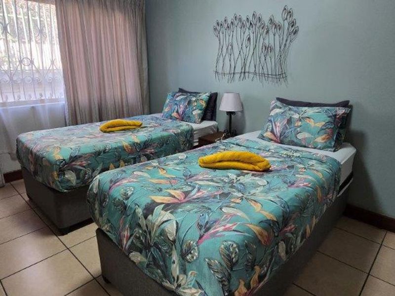 A functional bedroom featuring tiled flooring and a window fitted with security bars, providing a practical space for rest.
