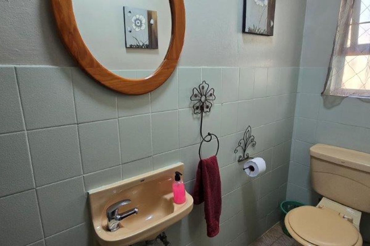 A compact guest bathroom featuring dated sanitaryware, wall-mounted basin, and tiled walls with a window providing natural light.