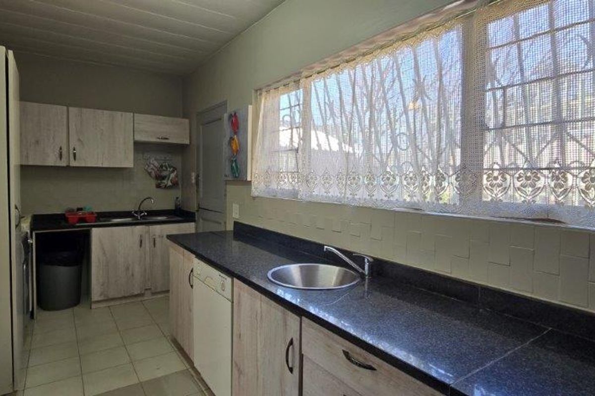 Functional kitchen featuring laminate cabinetry, dark granite countertops, stainless steel sink, and tiled flooring with security bars on the windows.