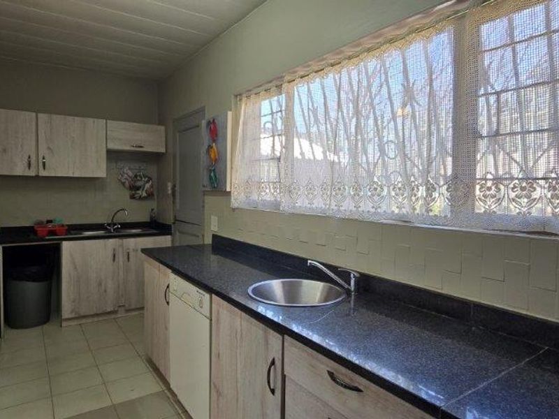 Functional kitchen featuring laminate cabinetry, dark granite countertops, stainless steel sink, and tiled flooring with security bars on the windows.