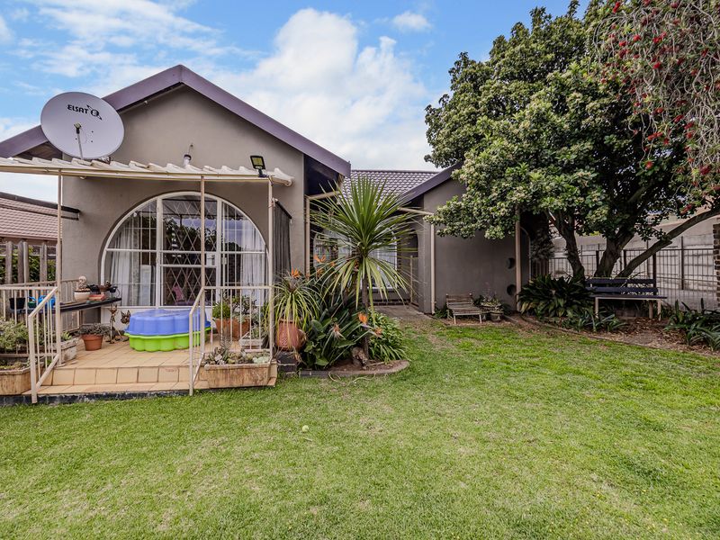 Rear view of the property featuring a tiled patio area, arched window, and a well-maintained garden with mature trees and boundary walling.