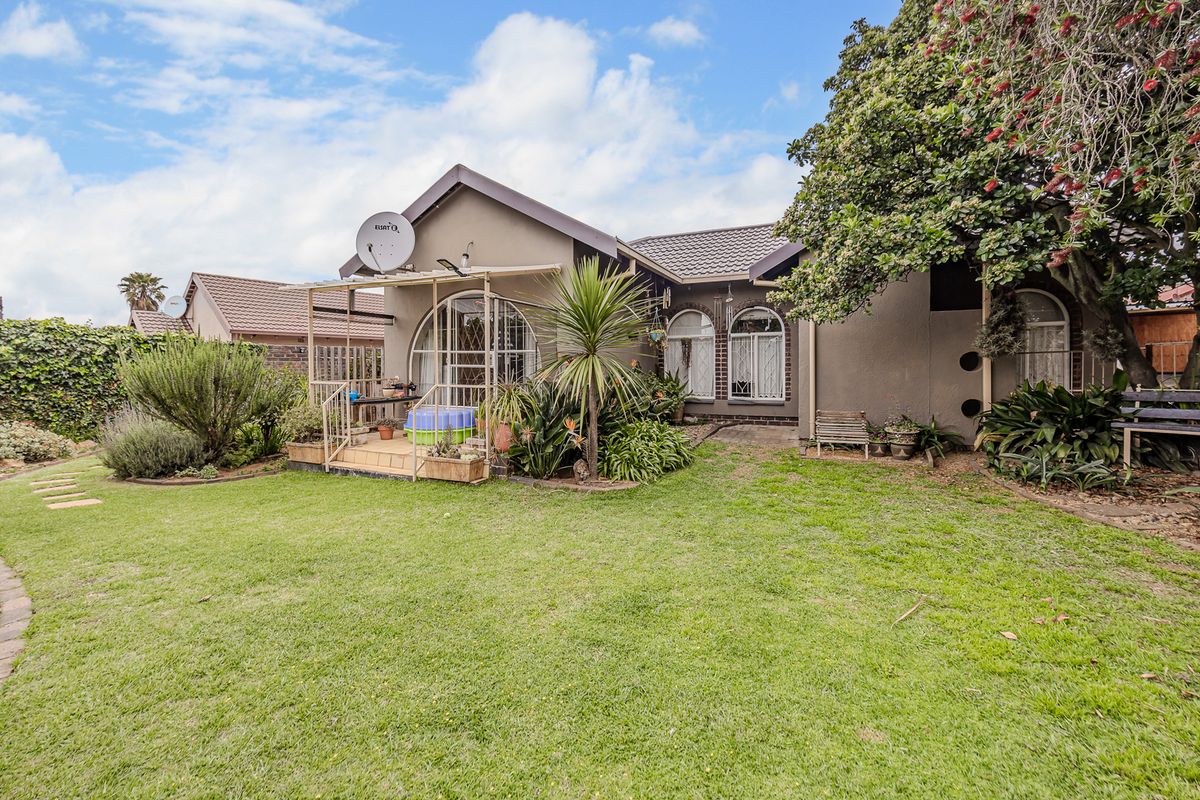 Rear view of the house featuring a well-maintained lawn, landscaped garden, and a covered patio area with arched window detailing.