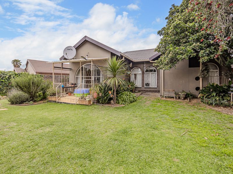 Rear view of the house featuring a well-maintained lawn, landscaped garden, and a covered patio area with arched window detailing.