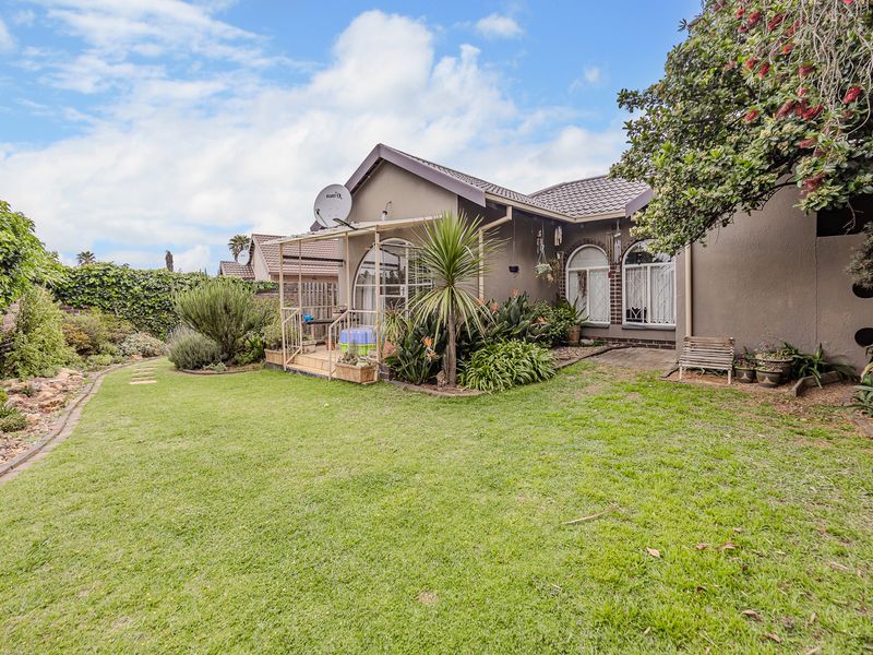 Rear view of the house featuring a well-maintained lawn, landscaped garden, and a covered patio area with arched window detailing.