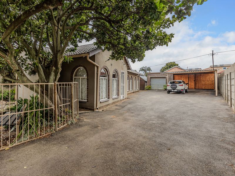 Front exterior view of the property featuring an asphalt driveway, arched windows, a garage, and a carport, enclosed by a boundary wall.