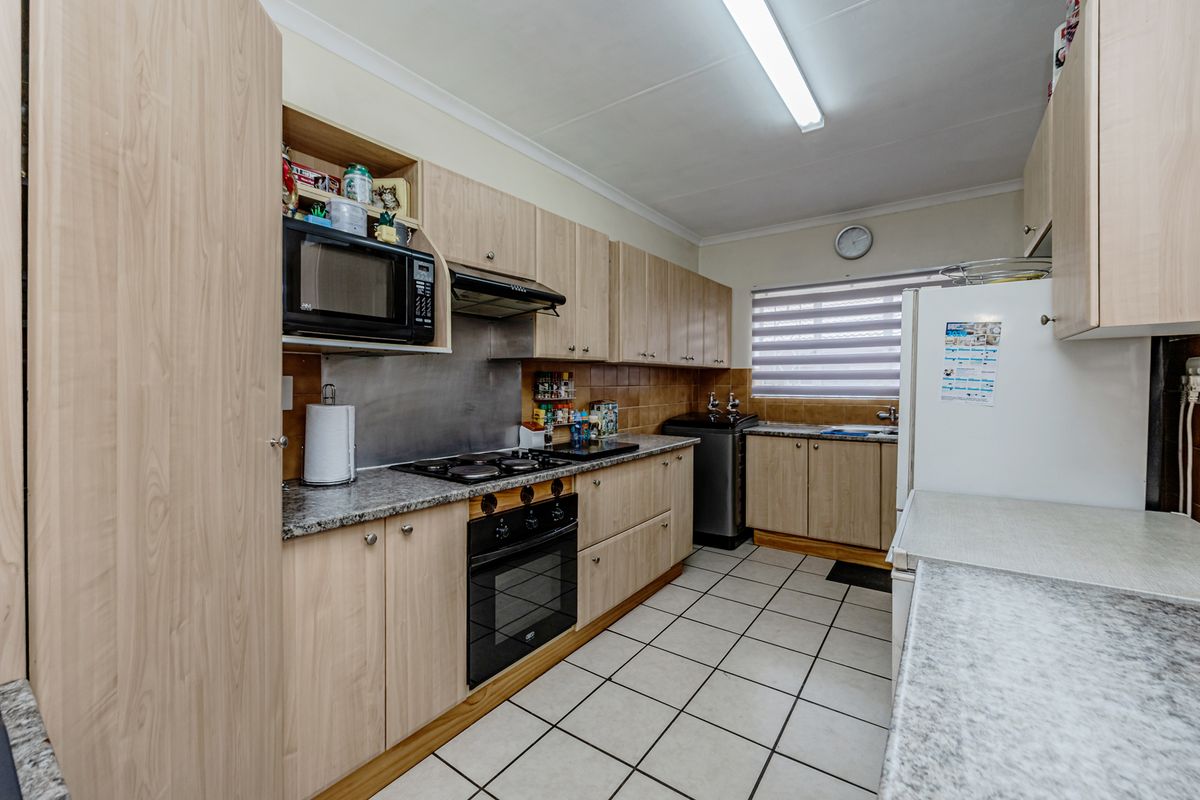Functional kitchen featuring light wood-finish cabinetry, laminate countertops, built-in oven with gas hob, extractor fan, and tiled flooring.