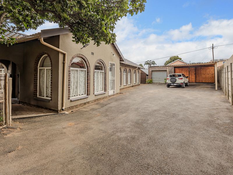 Spacious driveway leading to a house with arched windows, a garage, and a carport, enclosed by a precast concrete boundary wall.