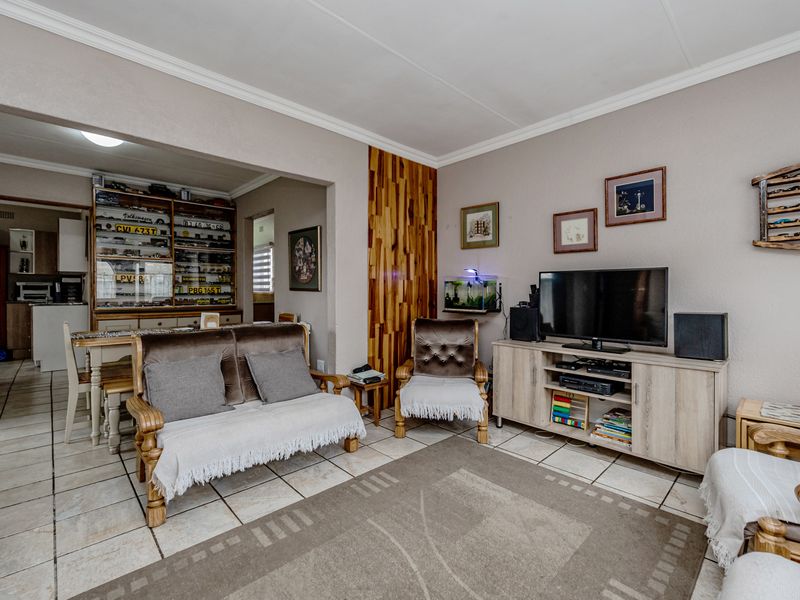 Open plan living area featuring tiled flooring, decorative wood wall paneling, and coved ceilings, with an adjacent kitchen visible in the background.