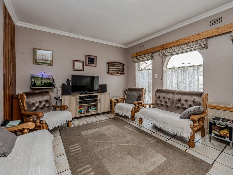 A comfortable living room featuring tiled flooring, arched windows with timber pelmets, and a built-in fireplace hearth, offering a functional and traditional living space.