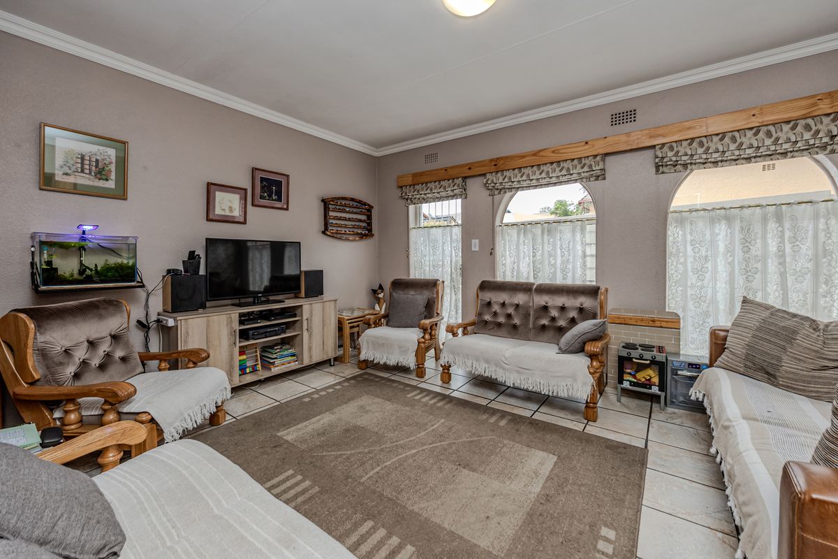 A comfortable living room featuring tiled flooring, coved ceiling cornices, and distinctive arched windows with timber pelmets.