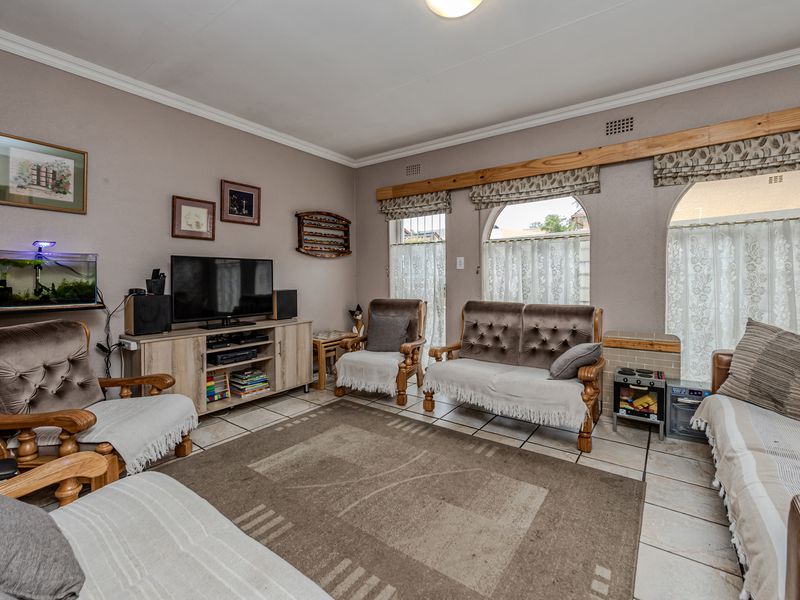 A comfortable living room featuring tiled flooring, coved ceiling cornices, and distinctive arched windows with timber pelmets.