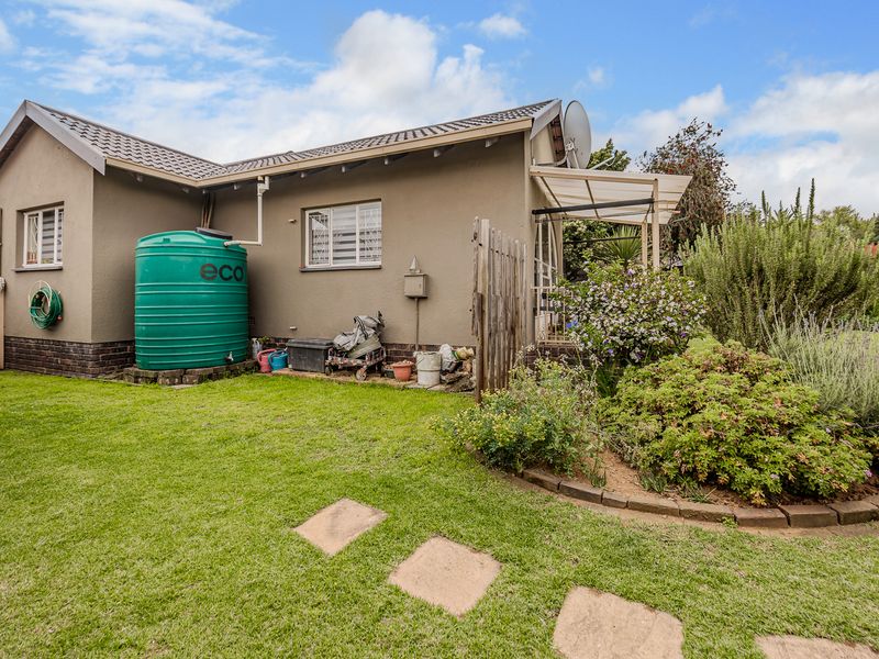 Rear view of the house featuring a landscaped garden, lawn, paved stepping stones, and a large water storage tank.