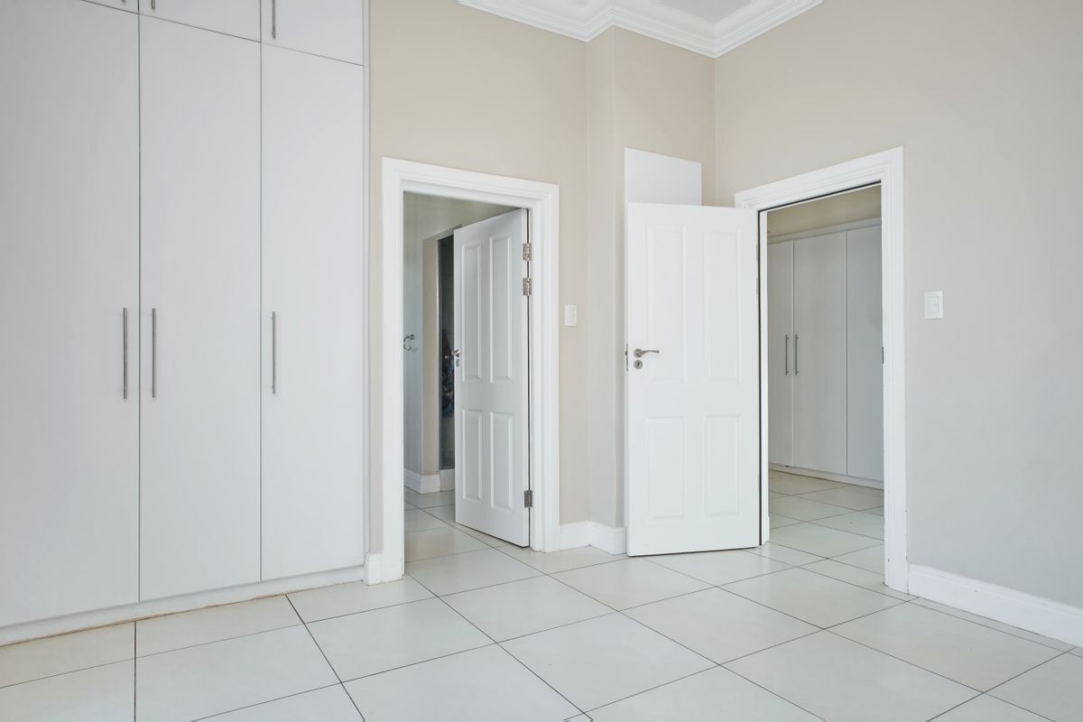 A bright, empty bedroom featuring neutral tiled flooring, built-in cupboards, and clean white internal doors leading to adjacent rooms.