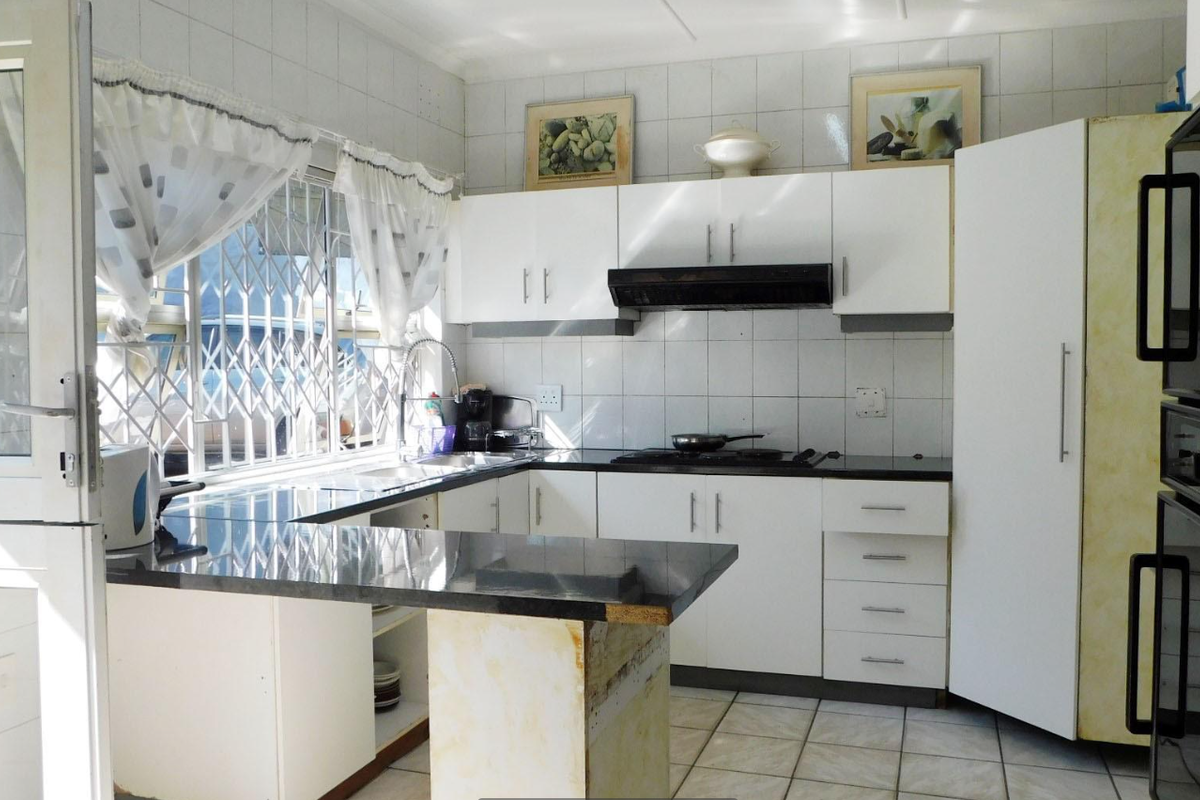 Functional kitchen featuring white cabinetry, granite countertops, built-in oven, extractor fan, and tiled backsplash with a security gate on the window.