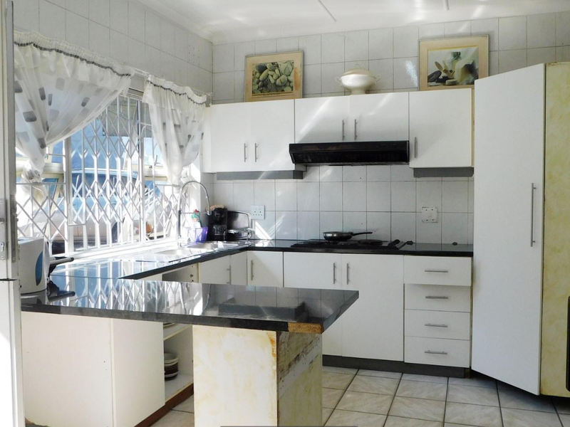 Functional kitchen featuring white cabinetry, granite countertops, built-in oven, extractor fan, and tiled backsplash with a security gate on the window.