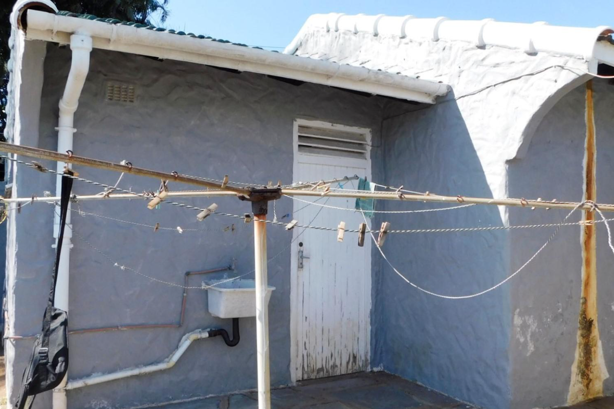 Rear exterior view of the property featuring a utility sink, external plumbing, and a weathered door entrance.