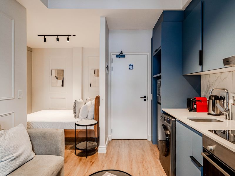 Modern open-plan studio apartment featuring a compact kitchen with blue cabinetry, integrated appliances, and a seamless transition to the bedroom and living area.
