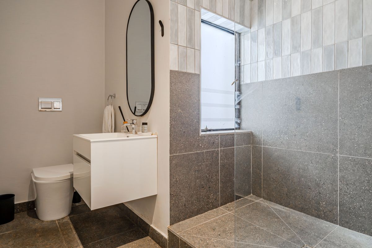 Modern bathroom featuring a walk-in shower with glass screen, wall-hung toilet, and a sleek wall-mounted vanity with contemporary tiling.