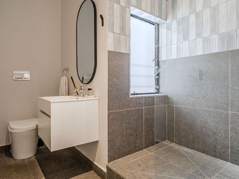 Modern bathroom featuring a walk-in shower with glass screen, wall-hung toilet, and a sleek wall-mounted vanity with contemporary tiling.