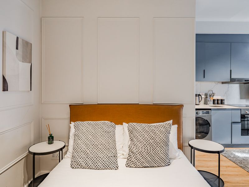 A modern open-plan studio apartment featuring elegant wainscoting, a contemporary blue kitchen with integrated appliances, and high-quality finishes throughout.