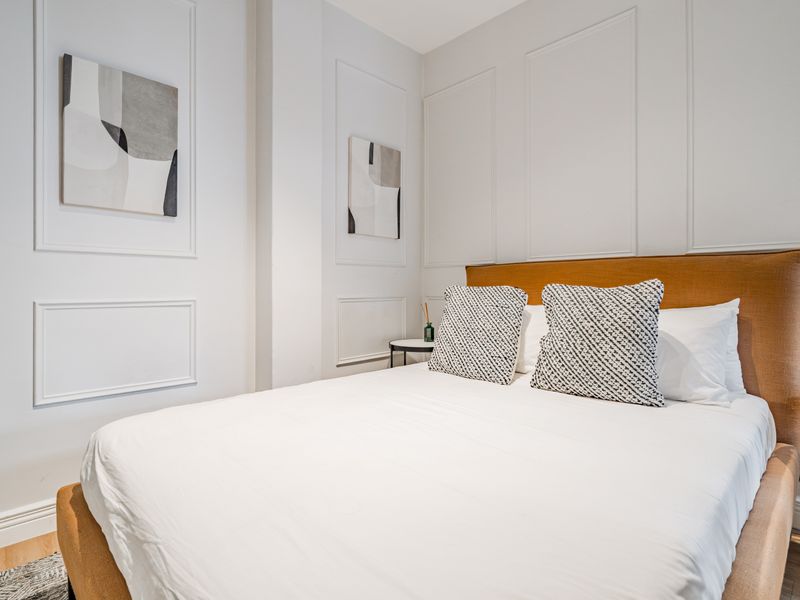 A well-maintained bedroom featuring elegant wall wainscoting, hardwood flooring, and clean, neutral finishes.