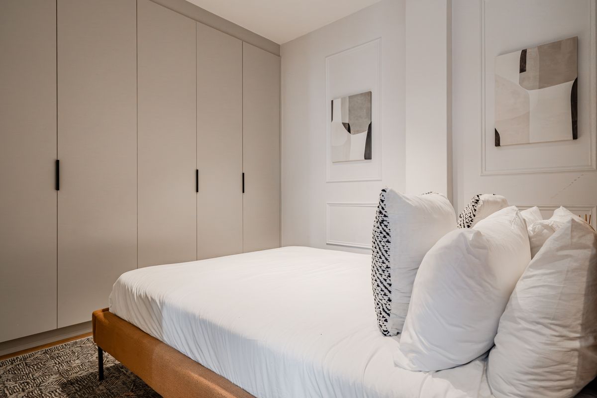 A modern, well-maintained bedroom featuring floor-to-ceiling built-in wardrobes and elegant wall molding details.