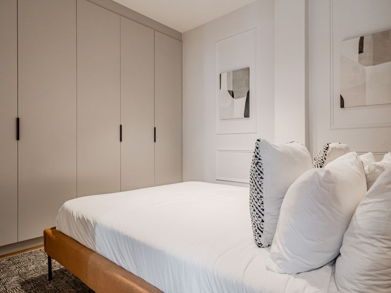 A modern, well-maintained bedroom featuring floor-to-ceiling built-in wardrobes and elegant wall molding details.