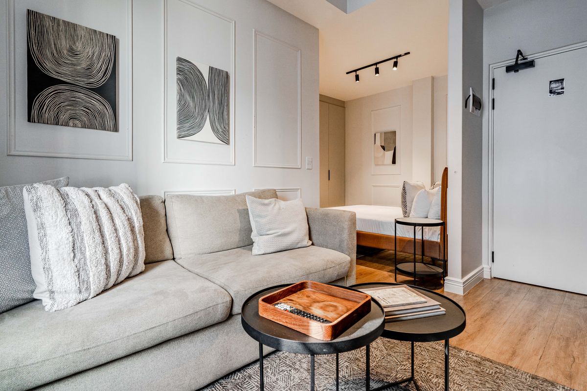 A modern open-plan living and sleeping area featuring elegant wall molding, track lighting, and high-quality laminate flooring in a well-maintained apartment setting.