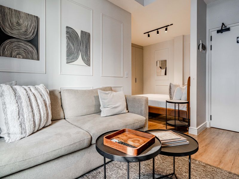 A modern open-plan living and sleeping area featuring elegant wall molding, track lighting, and high-quality laminate flooring in a well-maintained apartment setting.