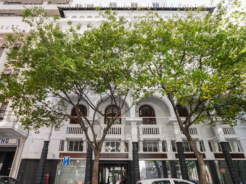 A well-maintained historic building facade featuring classic arched windows, decorative balustrades, and architectural columns, situated along a street with mature trees.