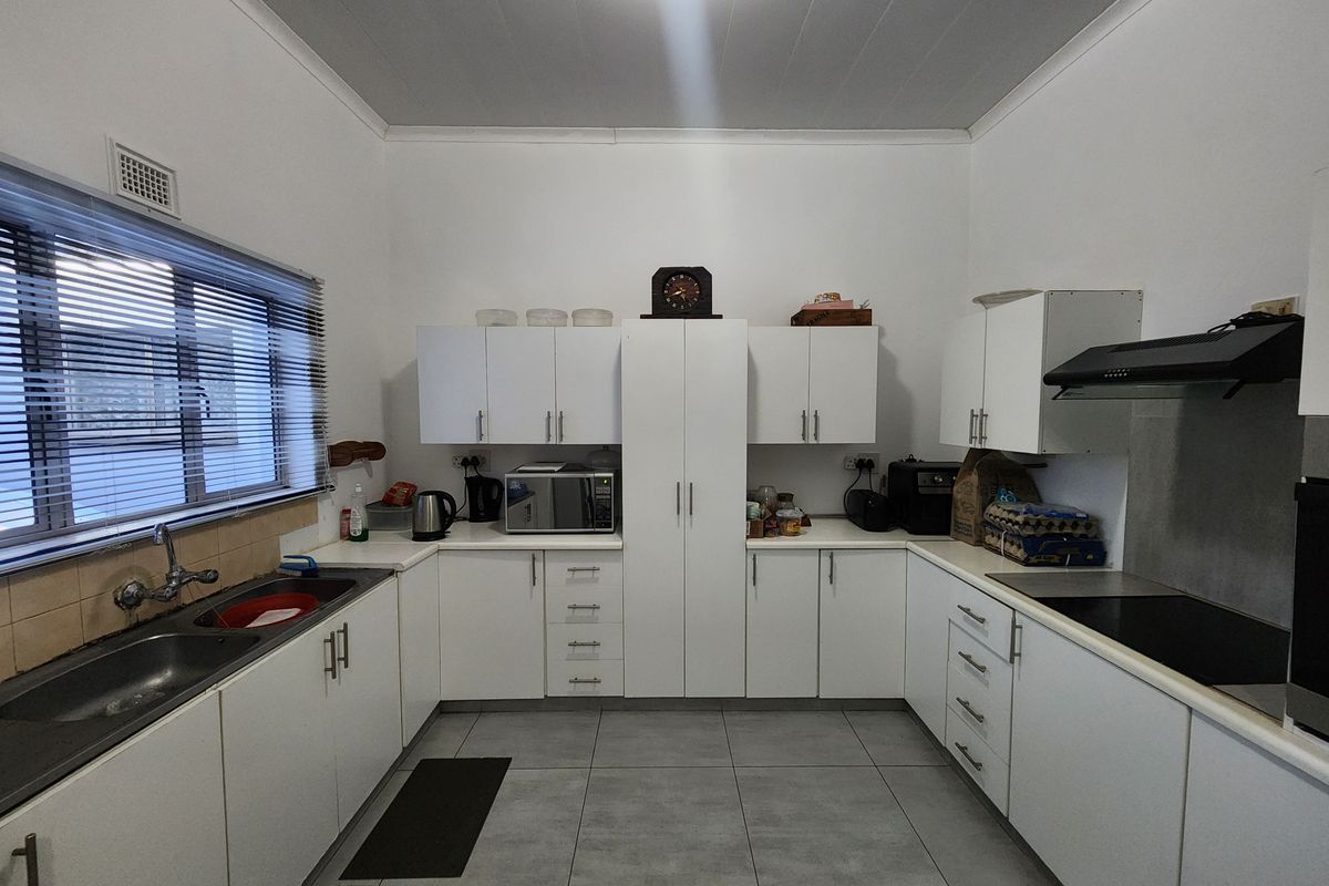 A functional kitchen featuring white built-in cabinetry, a double sink, a ceramic hob with an extractor fan, and modern grey floor tiles.